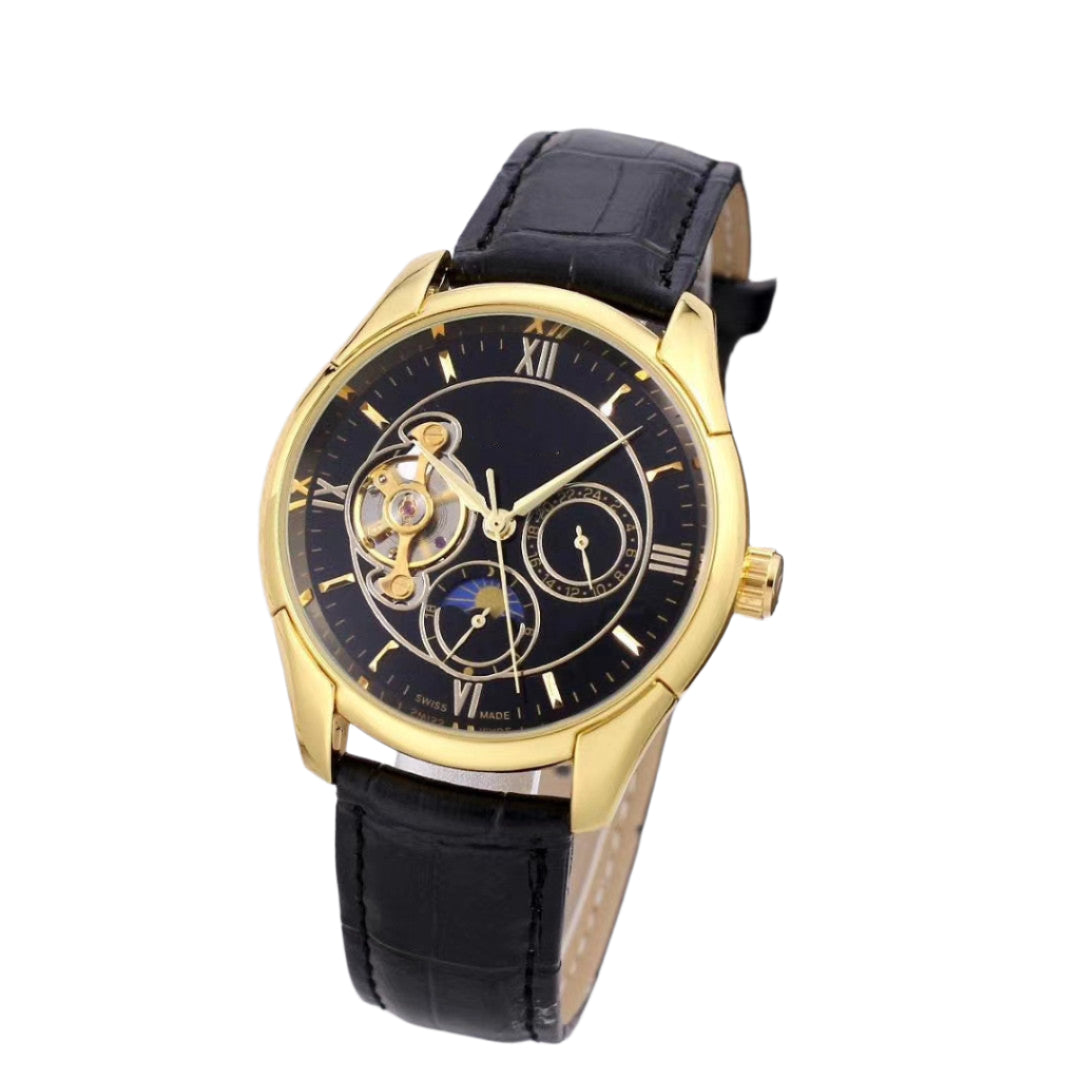 Luxury watch with black leather strap and gold case on a white surface with blurred keyboard and phone in the background